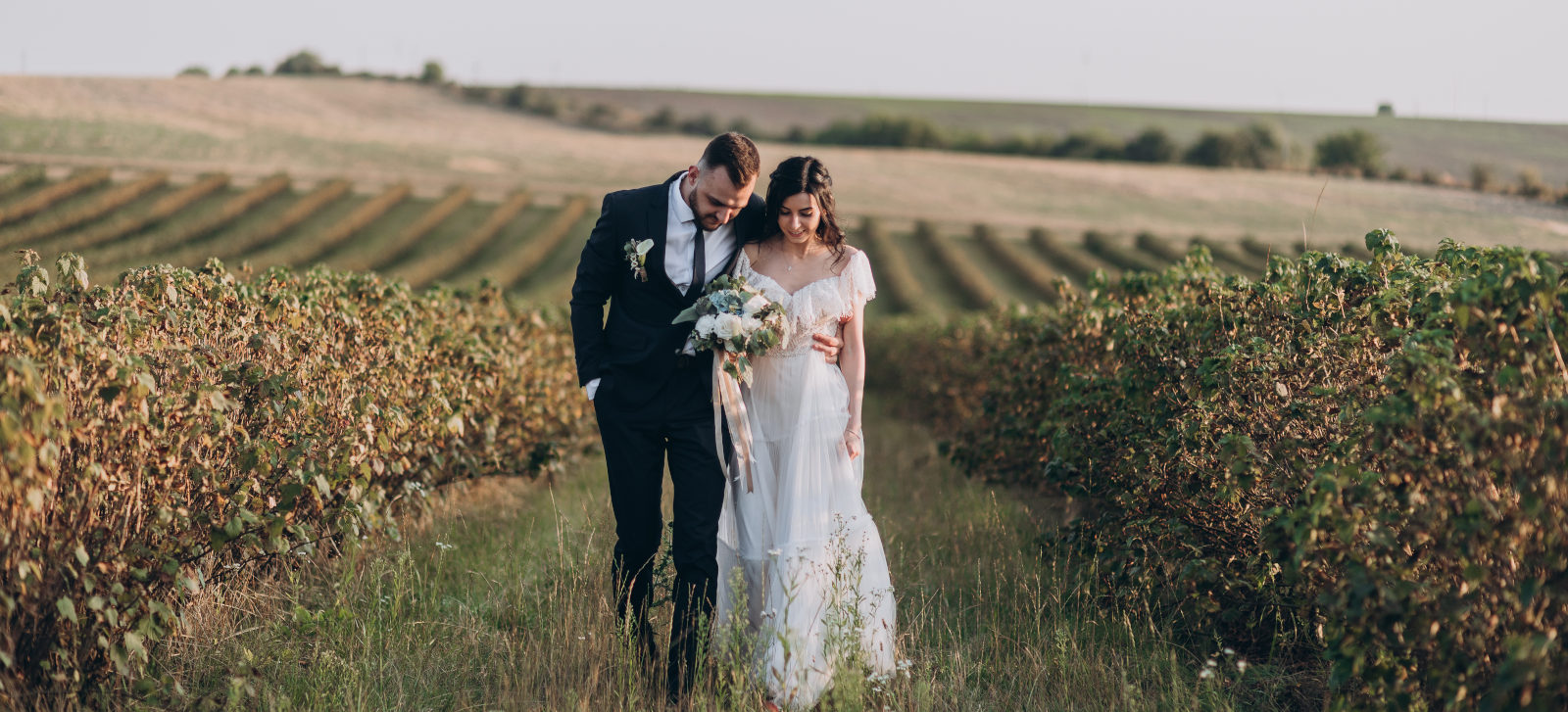 Glückliches Brautpaar geht auf einem großen Feld in der Toskana spazieren